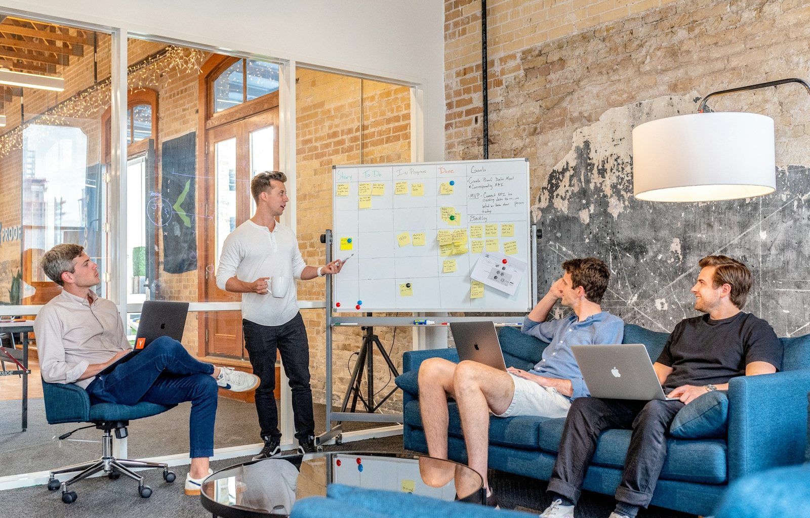 three men sitting while using laptops and watching man beside whiteboard