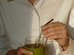 person in white button up shirt holding clear drinking glass with green liquid