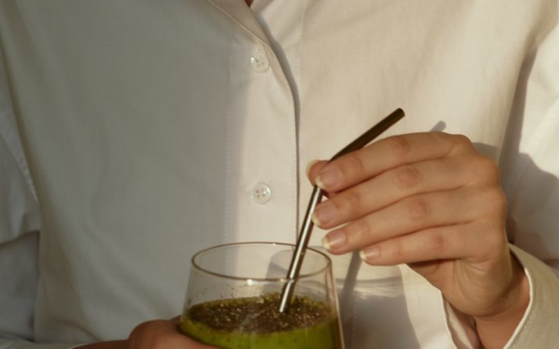 person in white button up shirt holding clear drinking glass with green liquid