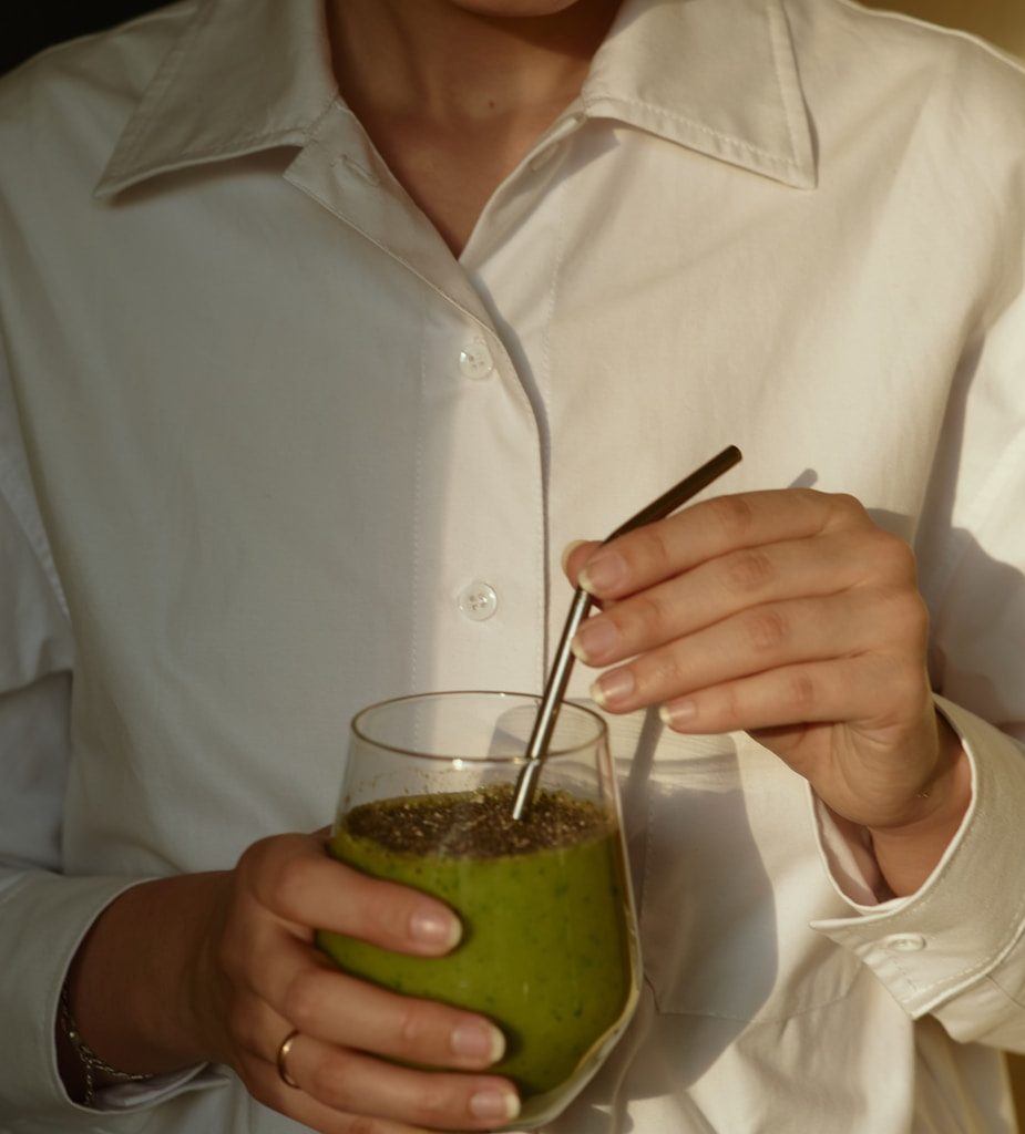 person in white button up shirt holding clear drinking glass with green liquid