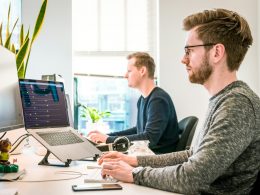 man sitting on chair wearing gray crew-neck long-sleeved shirt using Apple Magic Keyboard