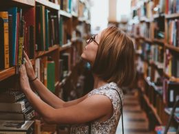 woman standing between library book shelves