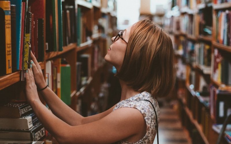 woman standing between library book shelves