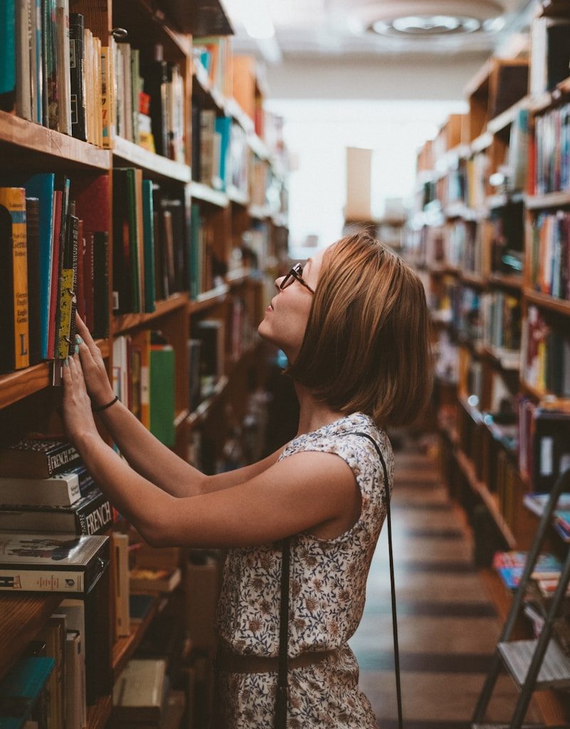 woman standing between library book shelves