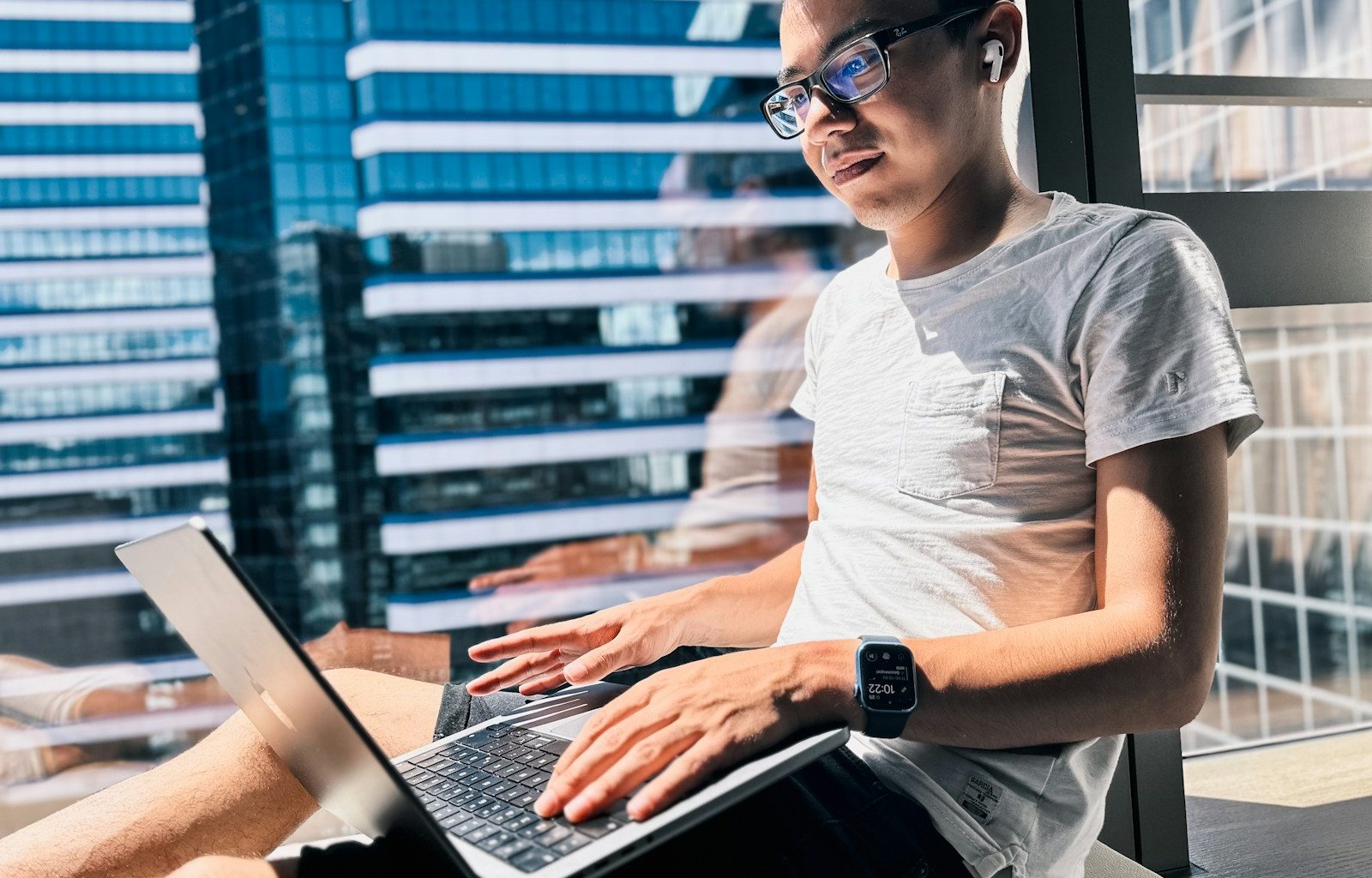 a man sitting in front of a window using a laptop computer