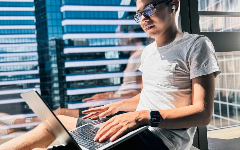 a man sitting in front of a window using a laptop computer