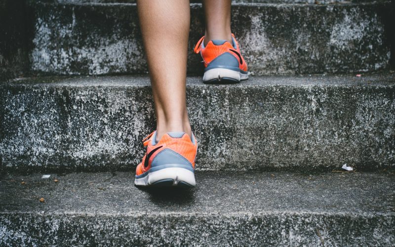 person wearing orange and gray Nike shoes walking on gray concrete stairs