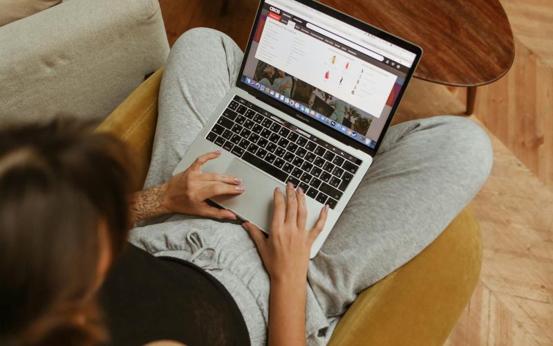 A person leisurely shopping online from home, using a laptop while sitting on a cozy chair.